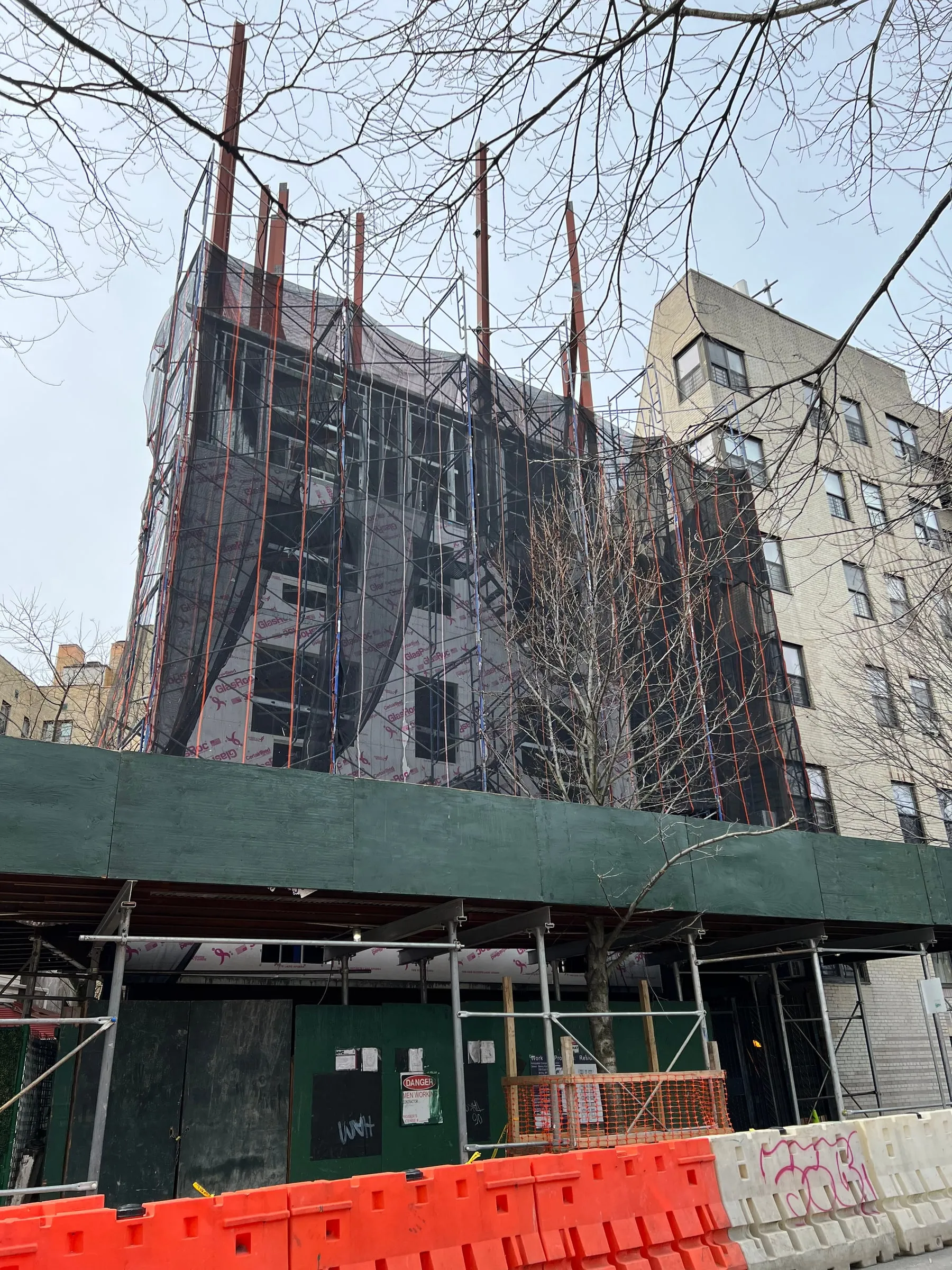 The same building under construction, netted and behind a sidewalk shed.