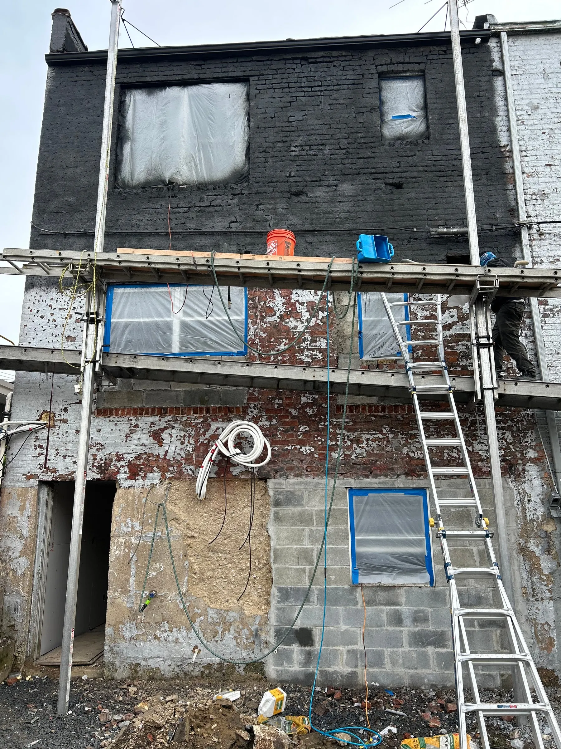 Scaffold up, openings sheeted and protected, and the base of the wall rebuilt in block.